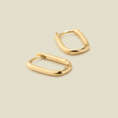 A pair of rounded rectangle hoop earrings, laying flat on a solid light beige surface.