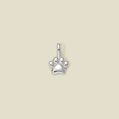 A silver polished paw print charm, centered on a solid beige background.