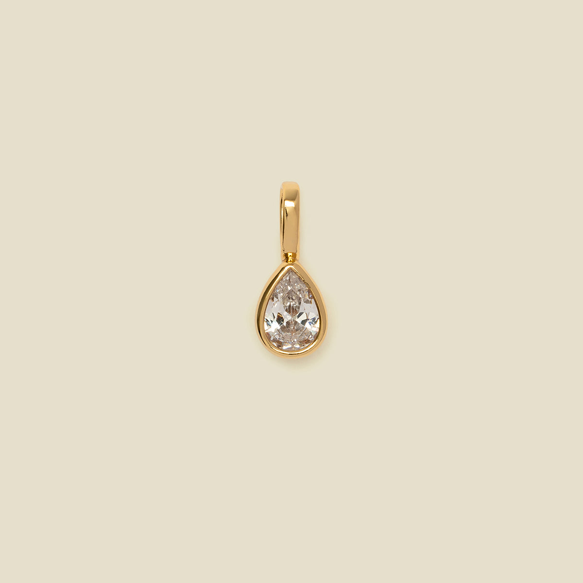 A gold teardrop-shaped pendant with a clear faceted gemstone, centered on a solid beige background.