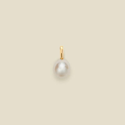 A pearl charm with a gold bail on a beige background