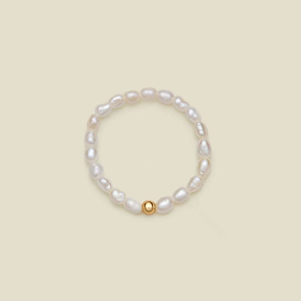 A beaded stretch ring featuring irregular white baroque pearls and a single polished gold bead accent, displayed on a solid light beige background.