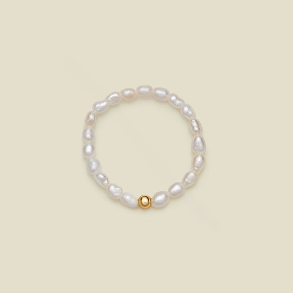 A beaded stretch ring featuring irregular white baroque pearls and a single polished gold bead accent, displayed on a solid light beige background.