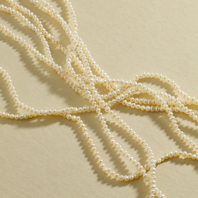 Multiple strands of pearls laying on top of each other, set against a textured beige background.