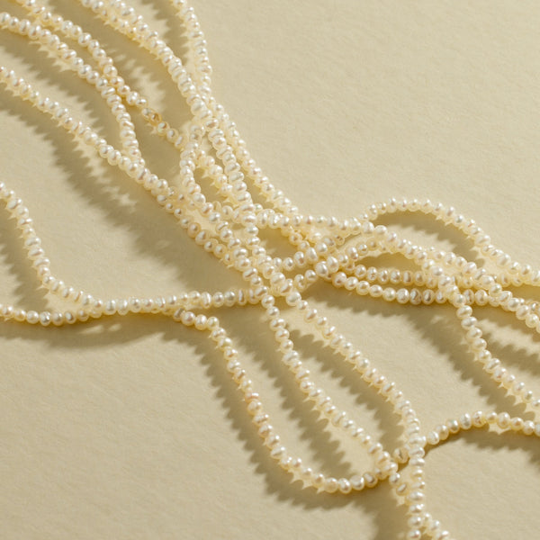 Multiple strands of pearls laying on top of each other, set against a textured beige background.