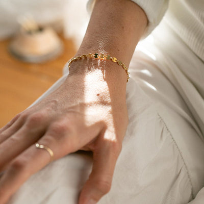 A close-up of a person's hand resting on their leg, showcasing a gold chain bracelet with flat round linked discs.