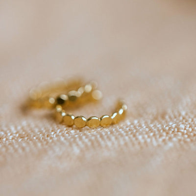 A gold textured cuff earring, laying on a beige linen background.