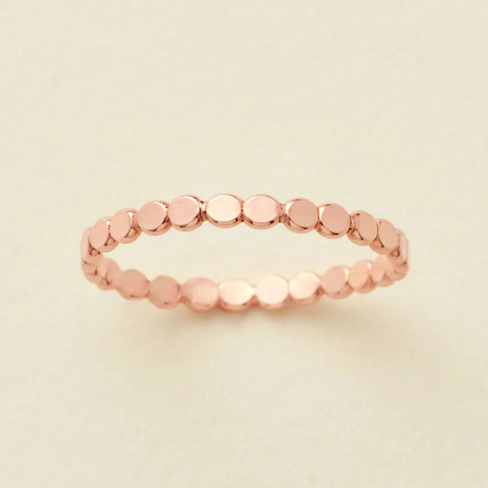 A thin rose gold band ring made of small, flat, circular disc-like links, photographed on a light beige background.