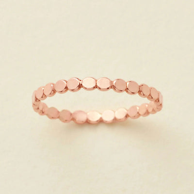 A thin rose gold band ring made of small, flat, circular disc-like links, photographed on a light beige background.