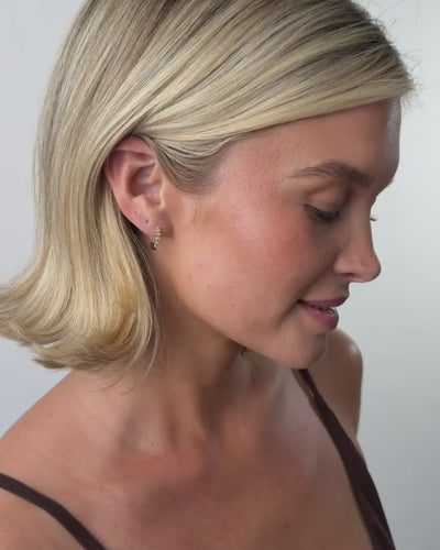 A short video of a blonde woman with a short bob wearing a gold hoop earrings made up of small bezel set round diamonds, set against a solid white background.