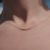 A short video of a person's neck wearing a delicate gold chain necklace featuring a short central crescent pattern with small clear baguette and round cut stones.