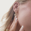 A short video of a woman's ear wearing a pair of polished gold hoop earrings, each with a dangling heart charm.