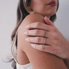 A short video of a model in a beige tank top wearing multiple stacked gold rings, each with a different color of square cut gemstones in a single continuous row.