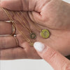 A short video of a hand holding three gold pendant chain necklaces, each with a peony flower engraved round flat disc pendant in different sizes. On the screen it has the measurements '1/4"', '3/8"', and '1/2"'.