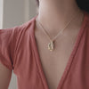 A short video of a close-up of a person in a red t-shirt wearing a gold chain necklace with an oval locket charm, a small rectangular bar engraved with the word 'LOVE', and a square red gemstone charm.