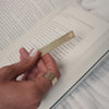 A short video of a person holding and using a gold engraved bookmark in a grey book.