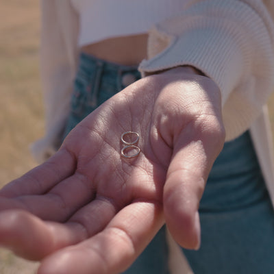 A short video of a woman holding a pair of small thin gold hoops in her palm, then showing her ear wearing a gold triangle stud made up of three bezel set clear gemstones and a small thin gold hoop.