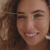 A short video of a model holding a delicate pendant chain with a gold hummingbird charm in front of their face, then wearing the necklace layered with a dainty pearl necklace.