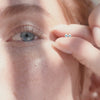 A short video of a woman holding two square bezel-set blue gemstone earrings in her fingers next to her blue eyes.