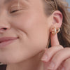 A close-up video of a woman showing her ears with two matching sets of polished gold chunky hoops in two different sizes, set against a light beige background.