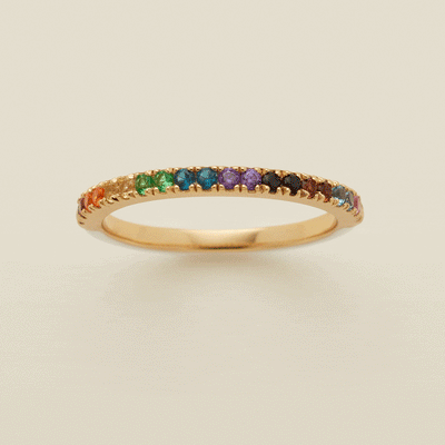 A gif of a delicate gold ring with a white enamel along the back half, and the pride rainbow of colors in small gemstones along the front. It is being shown from all angles.