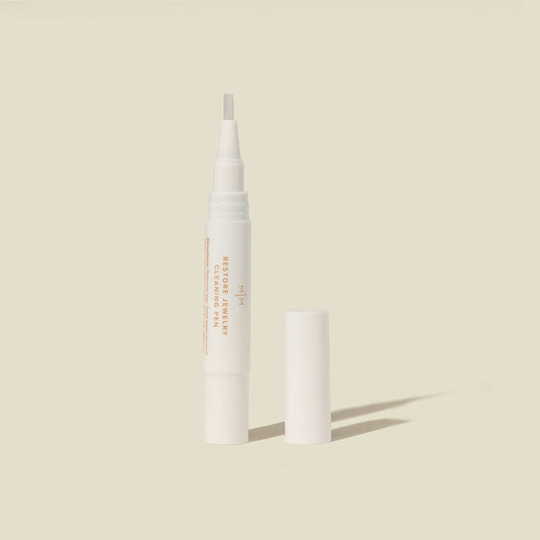 A white jewelry cleaner pen standing vertically with the cap off and placed beside it, shown on a solid light beige background.