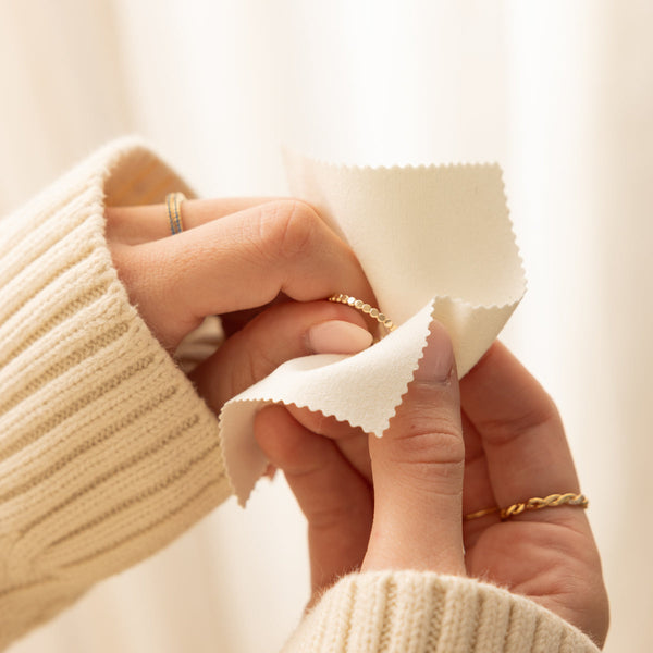 A person's hands holding a polished gold eternity ring and delicately touching it with a cream colored polishing cloth.