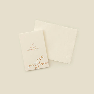 A square cream polishing cloth with a rectangular card on top with the words 'RESTORE POLISHING CLOTH', shown on a solid light beige surface.