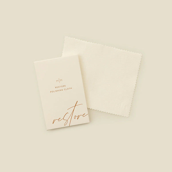 A square cream polishing cloth with a rectangular card on top with the words 'RESTORE POLISHING CLOTH', shown on a solid light beige surface.
