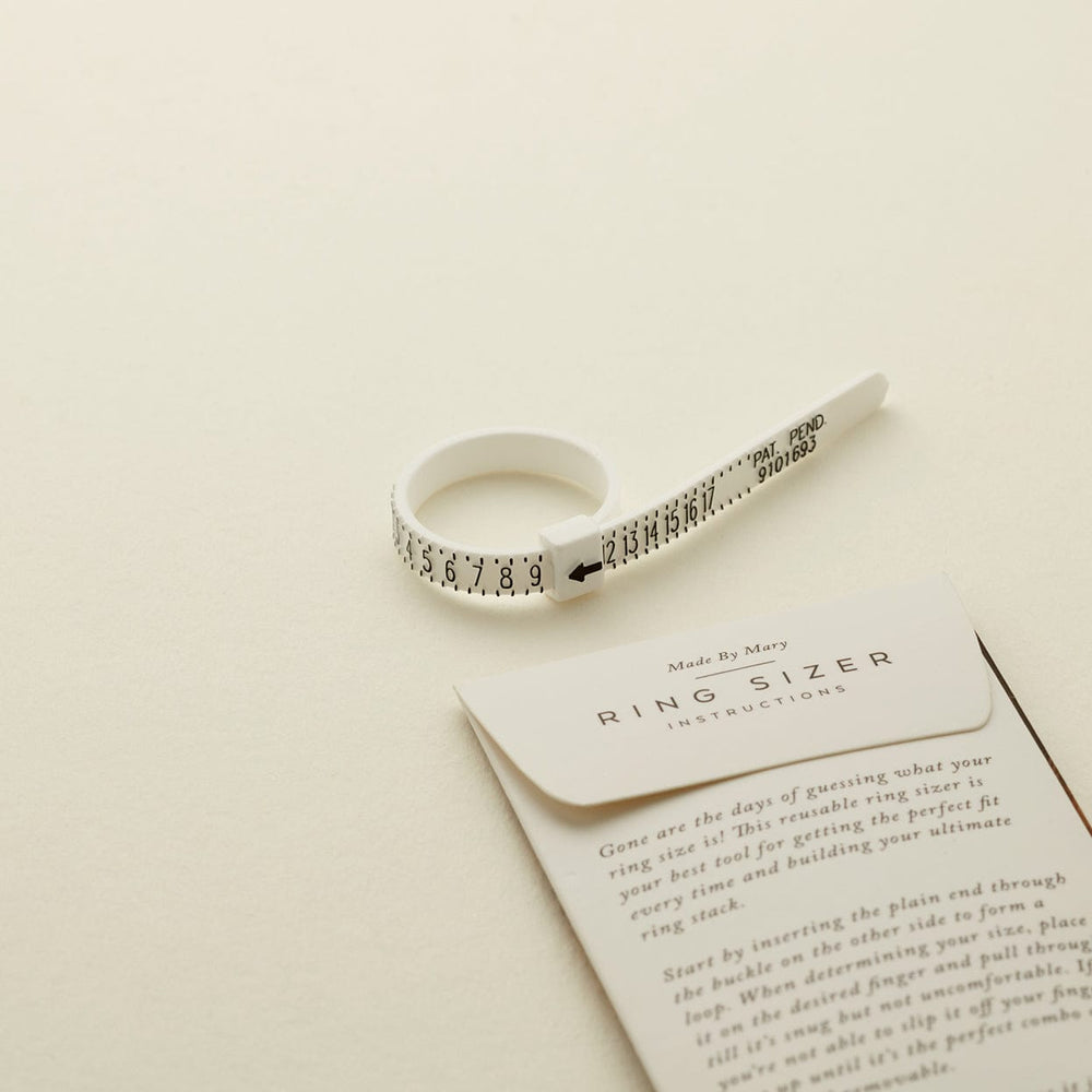 A white plastic zip-tie like ring sizer with black numbers, shown on a solid light beige surface.