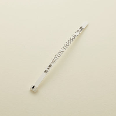 A single white plastic cable tie with black printed measurement markings and text, placed diagonally on a light beige background.