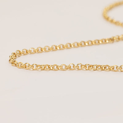 A close-up of a gold round link chain, laying on a solid white surface.