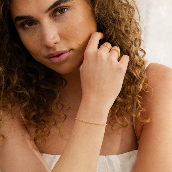 A person holding their hand to their face, showcasing their gold round link chain bracelet.