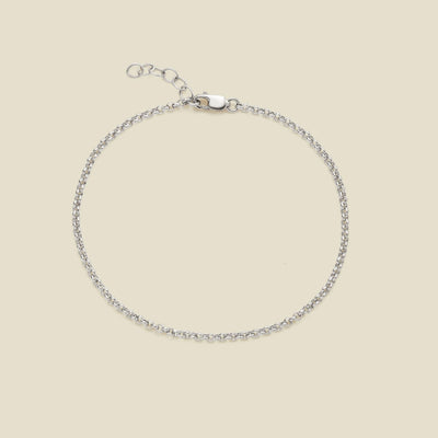 A delicate silver round link chain bracelet with a lobster clasp and extender chain, displayed on a solid light beige background.