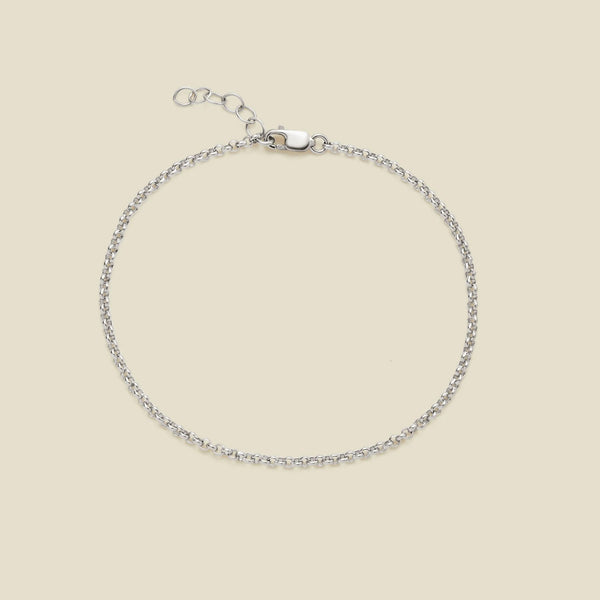 A delicate silver round link chain bracelet with a lobster clasp and extender chain, displayed on a solid light beige background.
