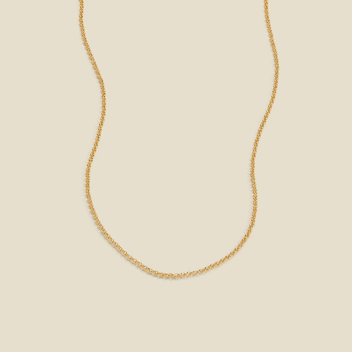 A delicate gold chain necklace with a round link pattern, displayed against a solid light beige background.