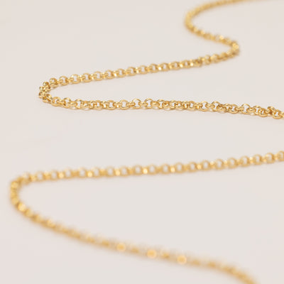 A round link gold chain necklace laid in a snaking pattern across a solid white surface.