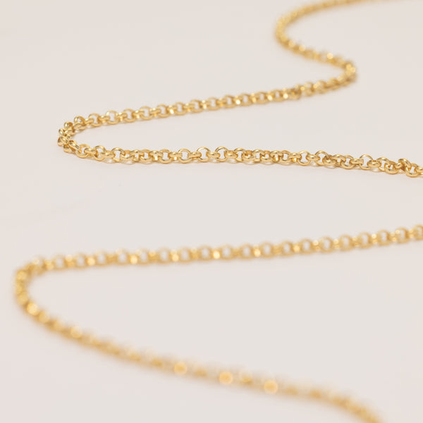 A round link gold chain necklace laid in a snaking pattern across a solid white surface.