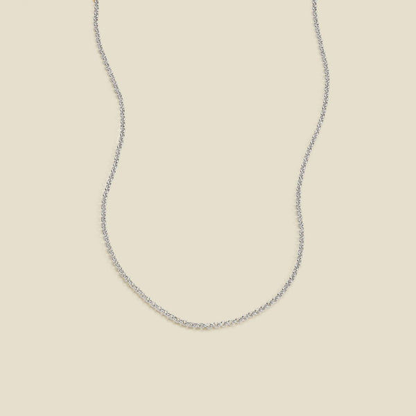 A delicate silver chain necklace with a round link pattern, displayed against a solid light beige background.