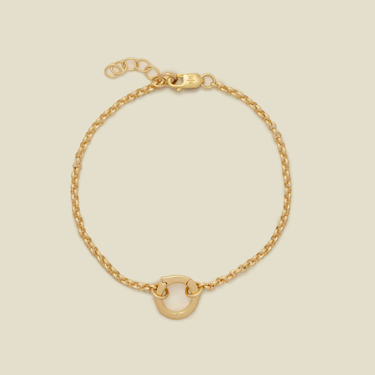 A delicate gold chain bracelet with a small polished gold O-ring at the bottom center, displayed on a solid light beige background.
