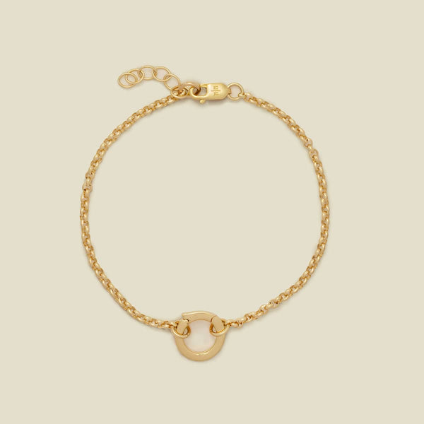A delicate gold chain bracelet with a small polished gold O-ring at the bottom center, displayed on a solid light beige background.