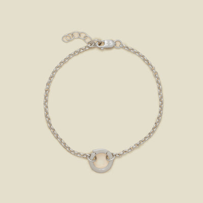 A silver circular link chain bracelet with a small round ring in the center, displayed on a light beige background.
