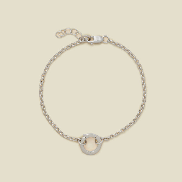A silver circular link chain bracelet with a small round ring in the center, displayed on a light beige background.