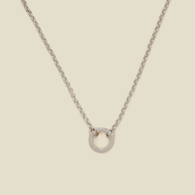 A silver circular link chain charm necklace with a hinge-style round ring in the center, displayed on a solid beige background.