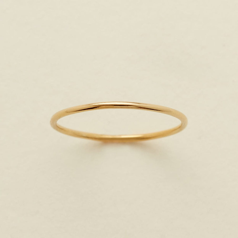 A minimalist, thin gold band ring centered on a warm, light beige textured background.