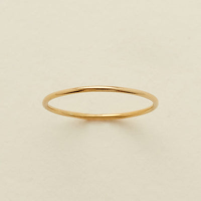 A minimalist, thin gold band ring centered on a warm, light beige textured background.