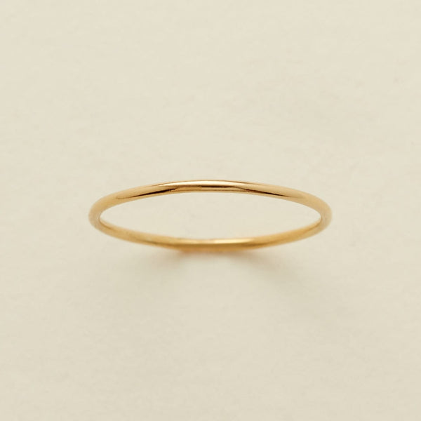 A minimalist, thin gold band ring centered on a warm, light beige textured background.