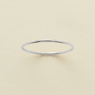 A thin round silver wire ring, shown on a solid light beige surface.