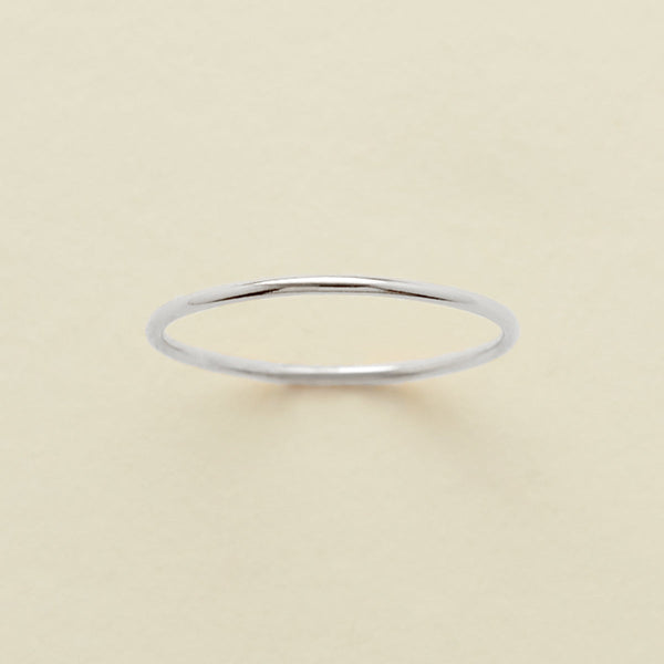 A thin round silver wire ring, shown on a solid light beige surface.