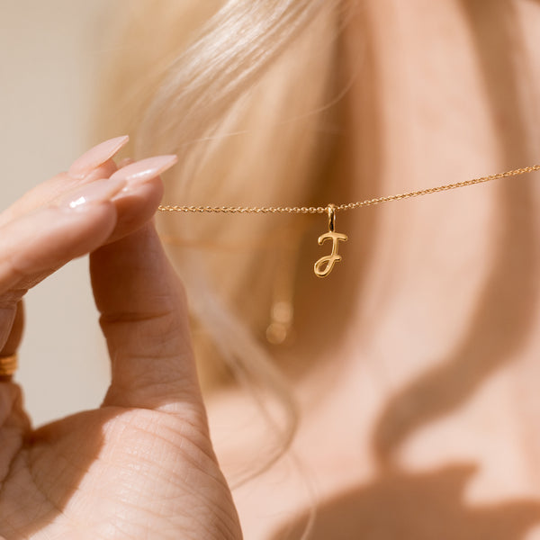 Close-up of a hand holding a delicate gold chain necklace with a small cursive "J" initial pendant.