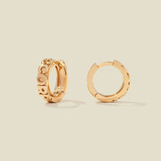 A pair of gold huggie hoop earrings on a light beige background. One earring is shown from the side, displaying a polished outer surface, while the other is shown from the front, showcasing the word 'SCORPIO' in raised letters.